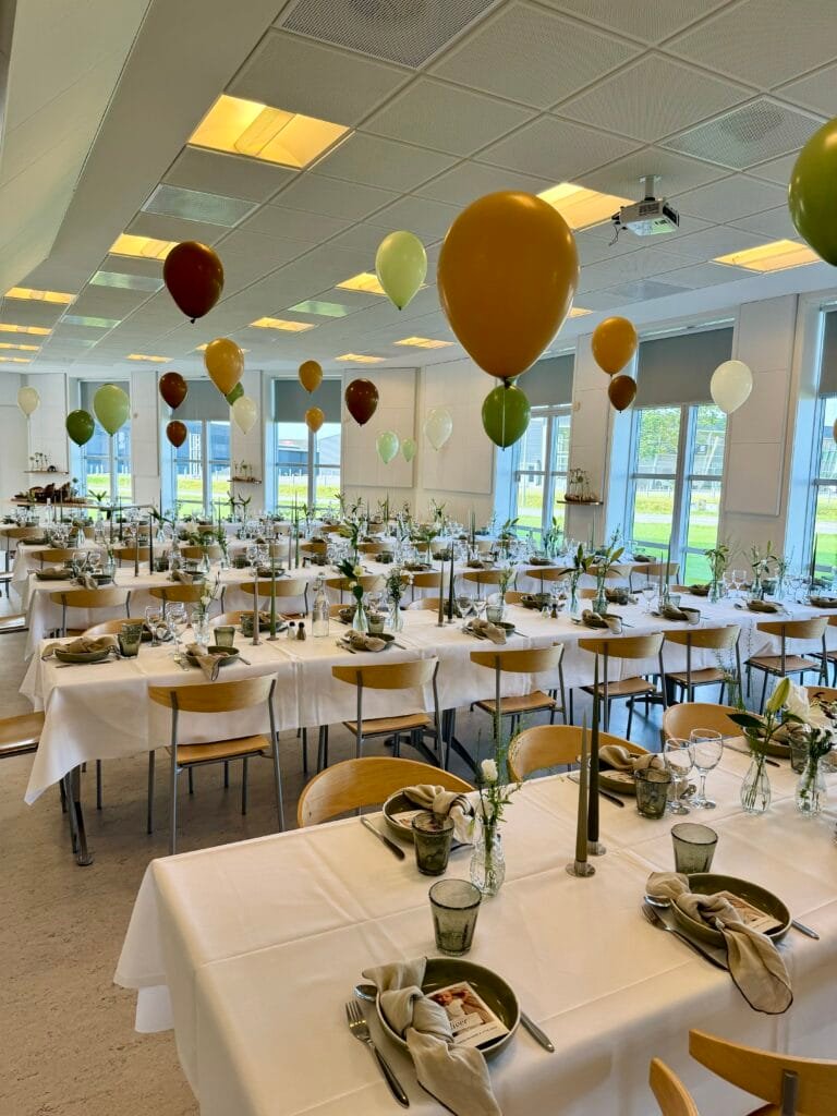 Festligt opdækket lokale med balloner og borde.