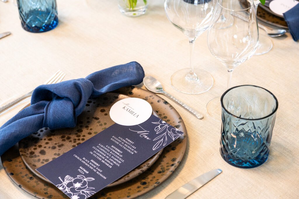 Elegant borddækning med blå serviet og menu.